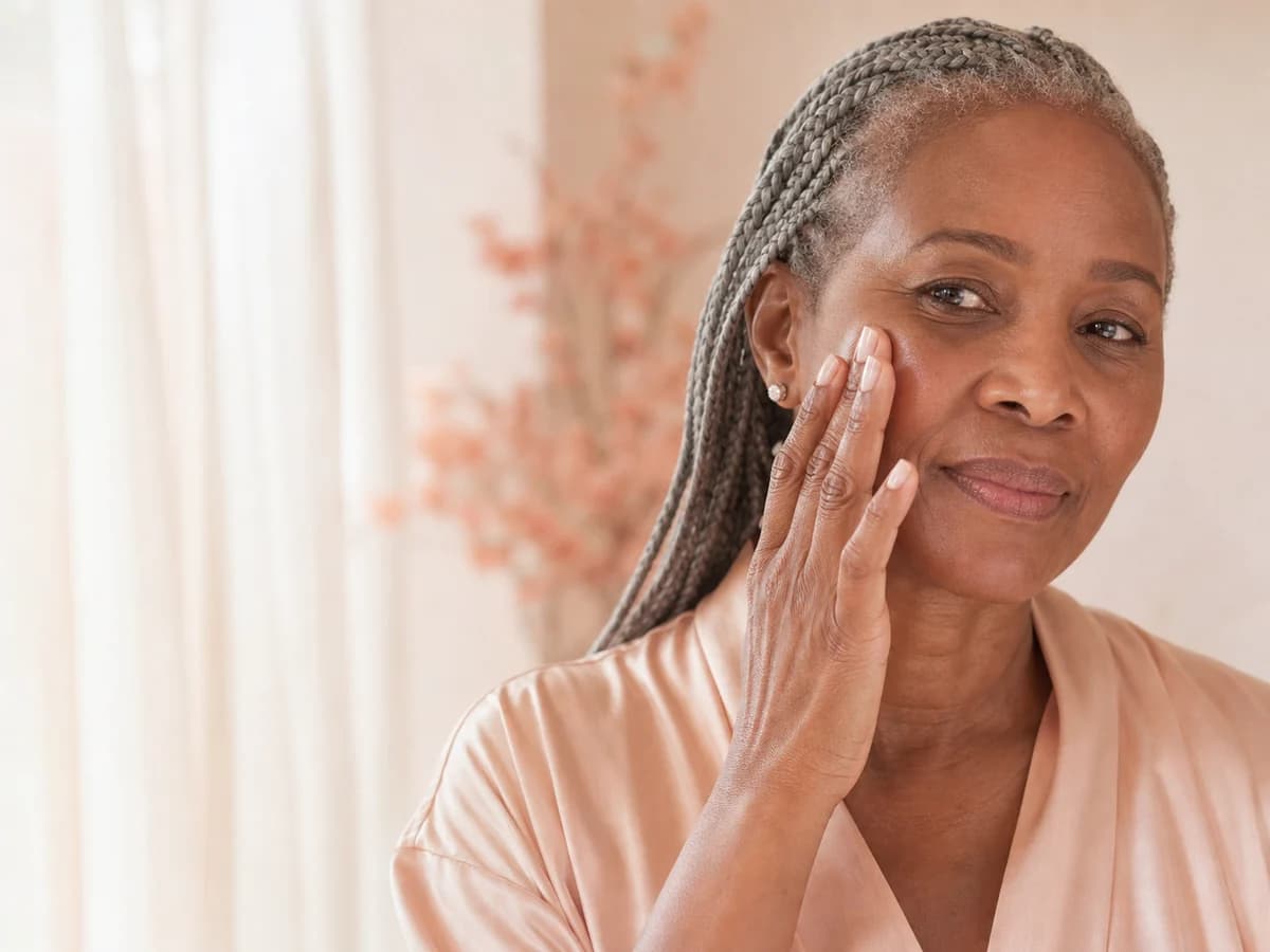 Older woman with silver braids touching her cheek in soft peach light