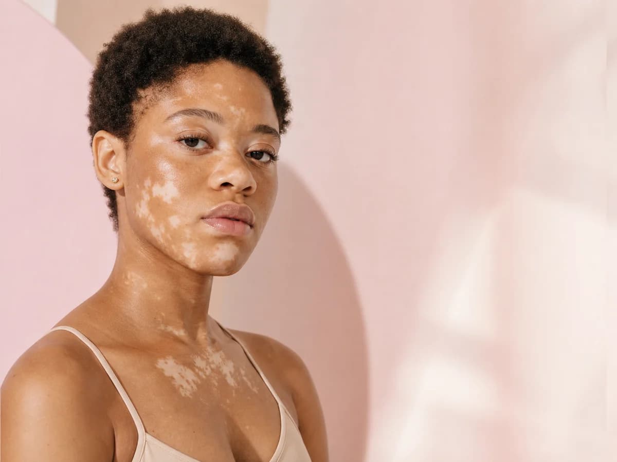 Person with short natural curls and varied skin pigmentation in soft pink light