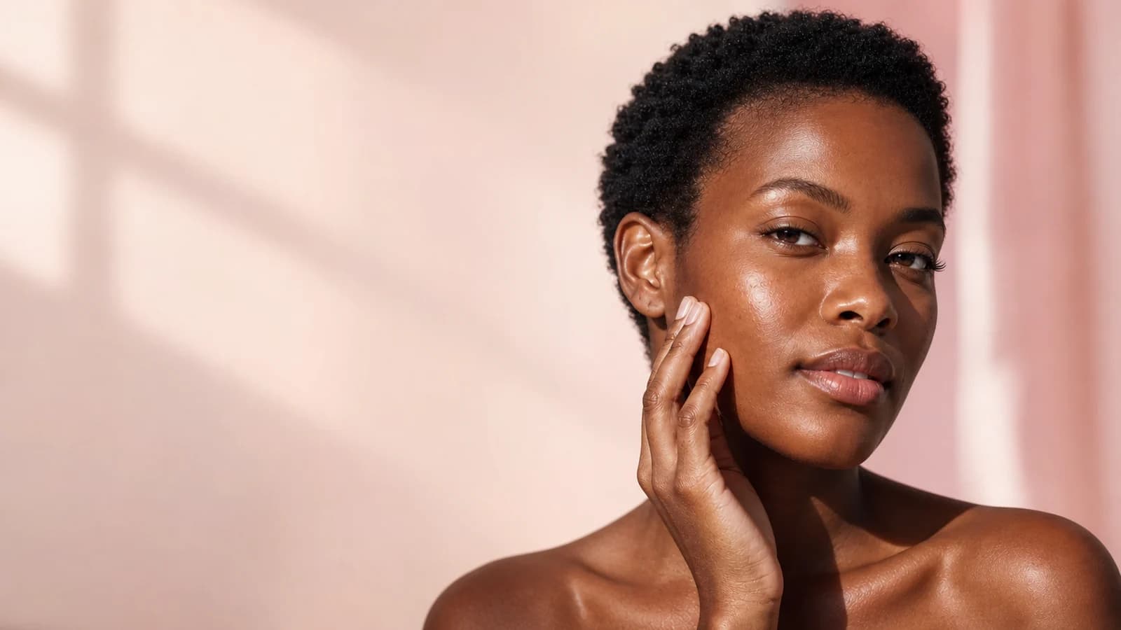 Woman with short natural hair touching her cheek against a peach backdrop