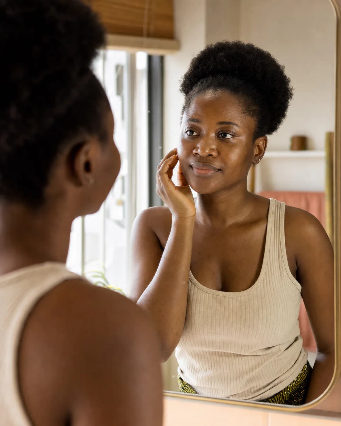 Nigerian woman calmly looking at her skin in a mirror