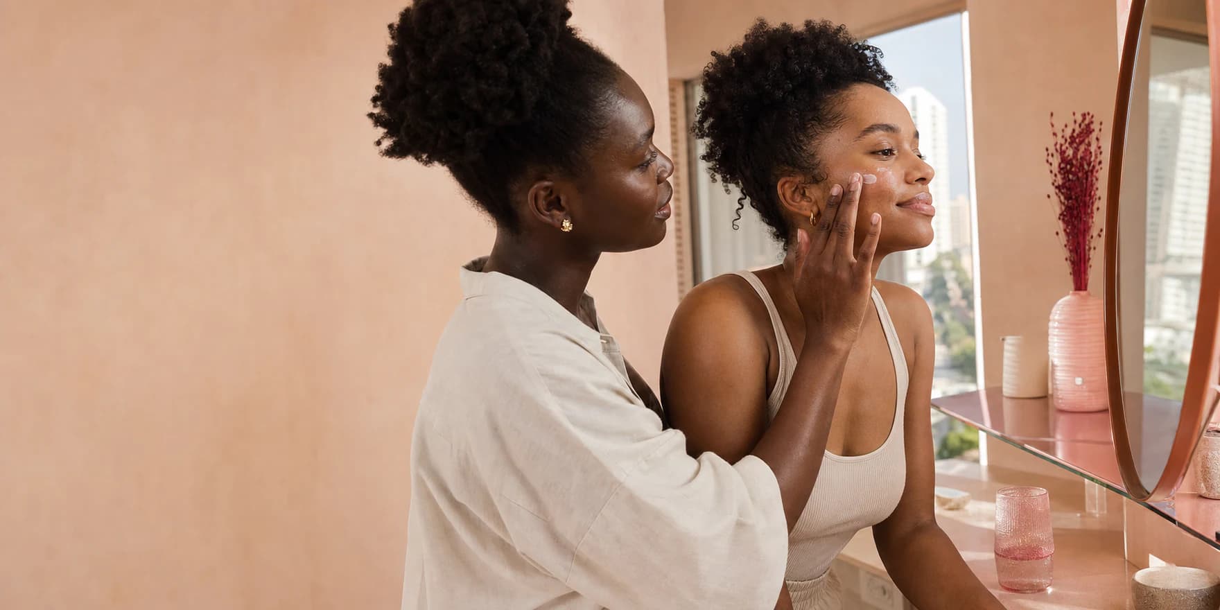 Two Nigerian friends sharing a quiet morning skincare moment in warm peach light
